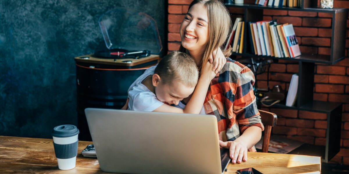 Mom and son laugh and hug, mom working from home. Student and teacher. (not a patient of ours that uses DENTAL IMPLANTS)