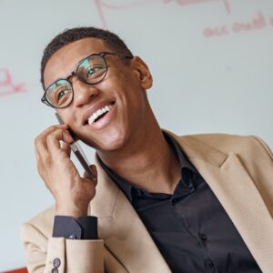 Smiling african businessman in glasses talking phone sitting in cozy coworking and looking away Smiling african businessman in glasses talking phone sitting in cozy coworking and looking away