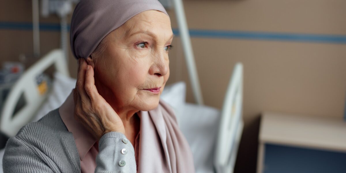 upset senior woman with cancer sitting on bed in hospital TranscenDental Smiles Provids ORAL CANCER SCREENING services