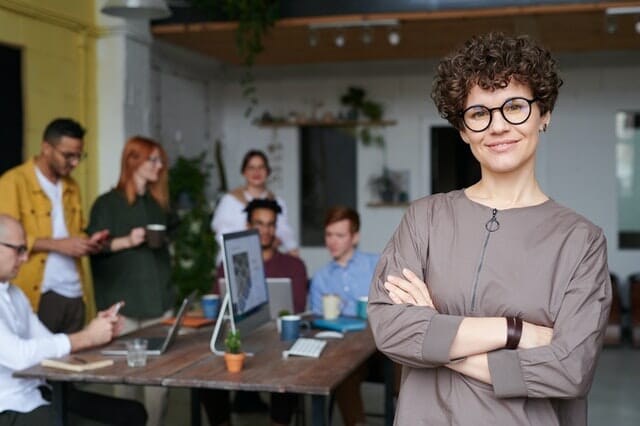 A woman with glasses confidently addressing a group of people.