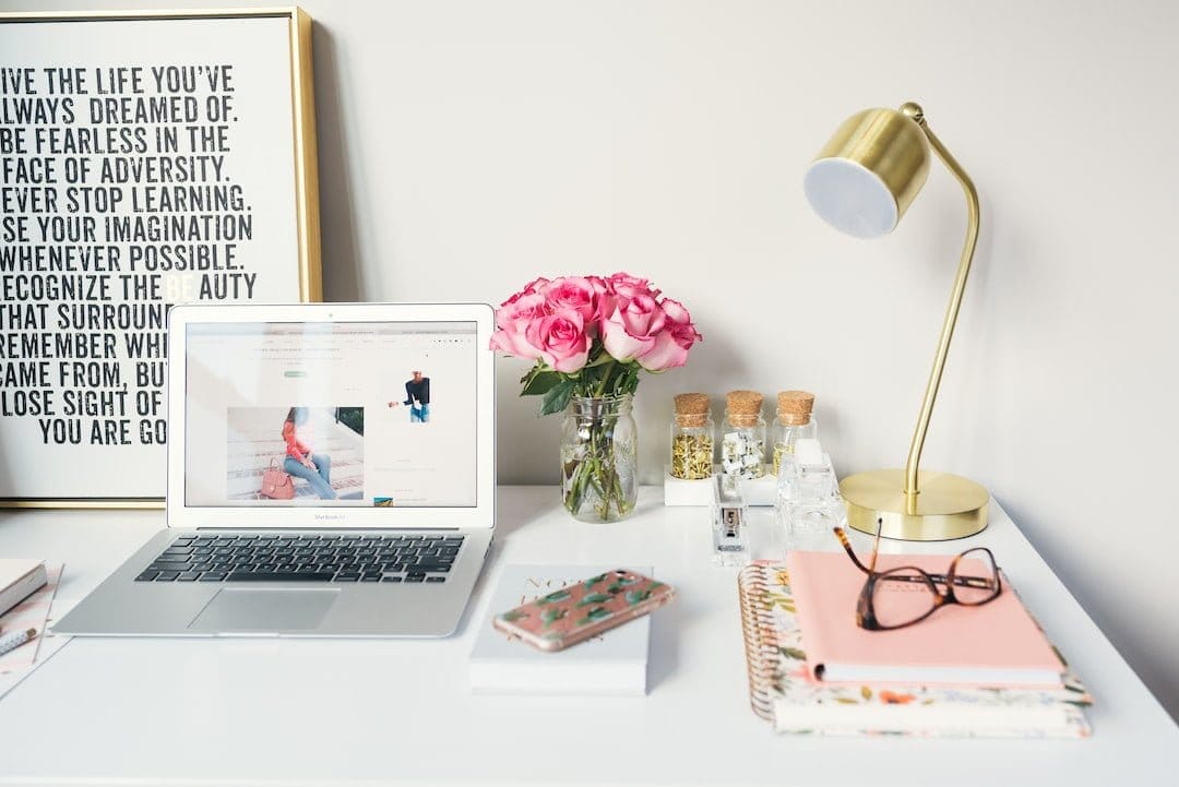 A desk with a laptop, flowers, and a framed quote. A workspace adorned with nature and inspiration.