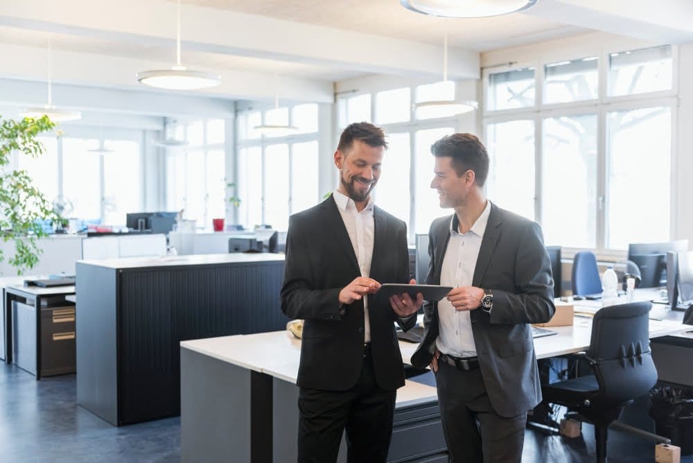 Two businessmen in suits standing in a modern office, discussing business matters and looking professional.