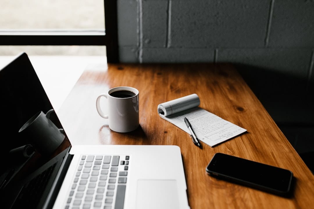 A laptop sits on a wooden desk next to a cup of coffee.