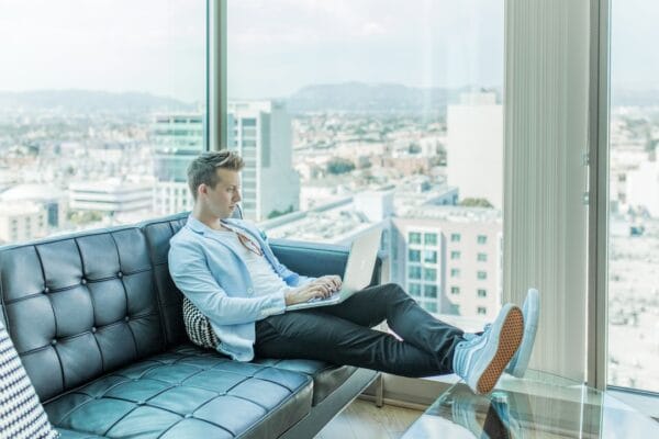 A man sitting on a couch with a laptop in front of a city view.