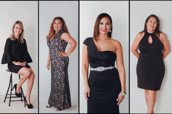 Four women in elegant black dresses posing together for a group photo.